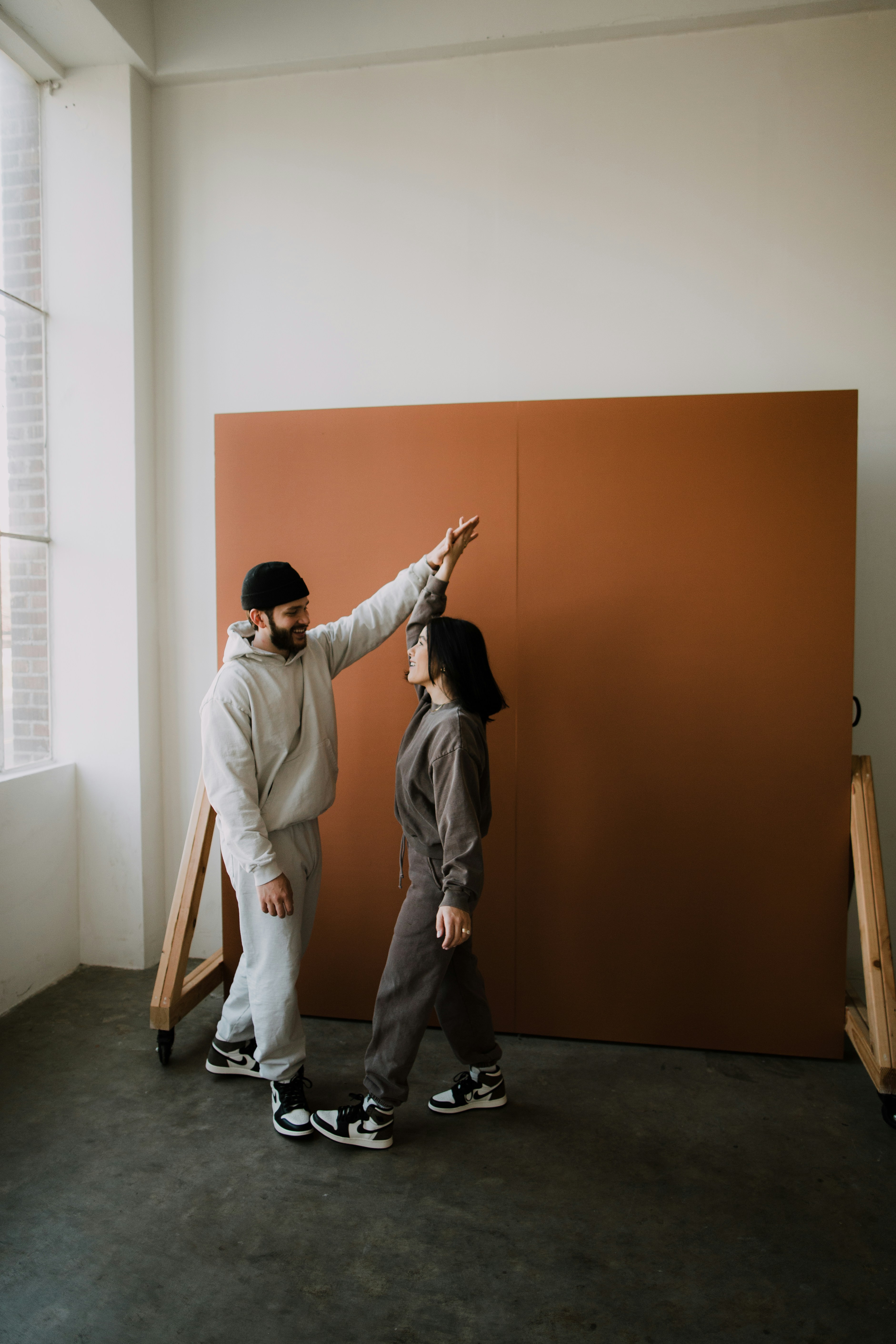 A couple in sweatsuits dances in front of an orange backdrop while smiling at each other