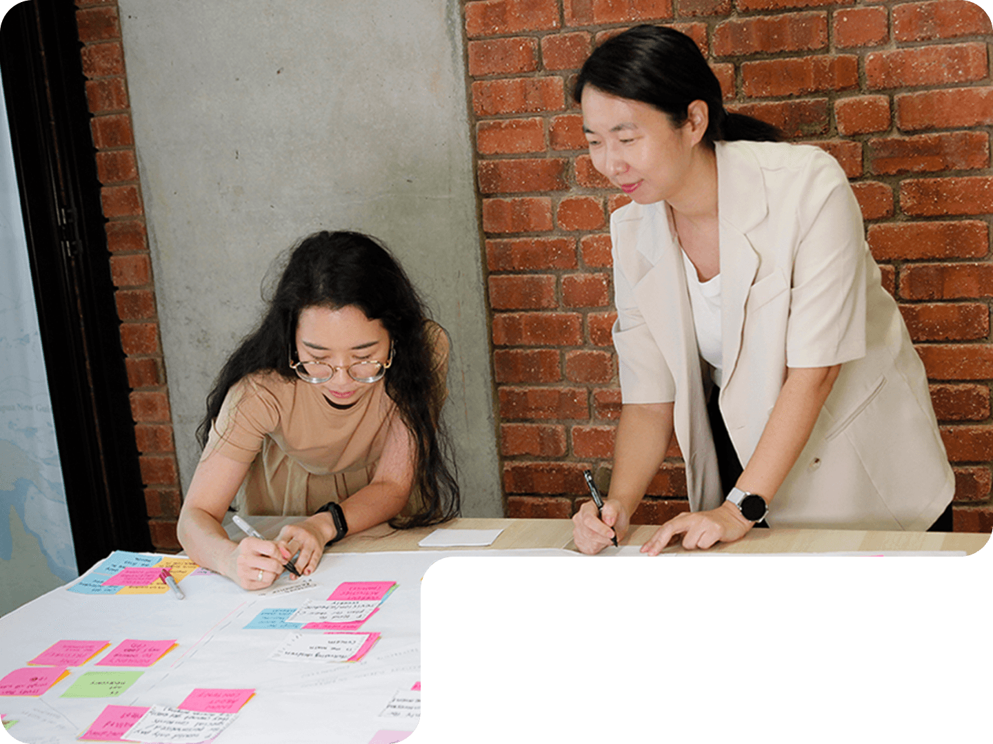 Two members of 55 Minutes collaborating at a table, writing on a large sheet filled with colorful sticky notes.