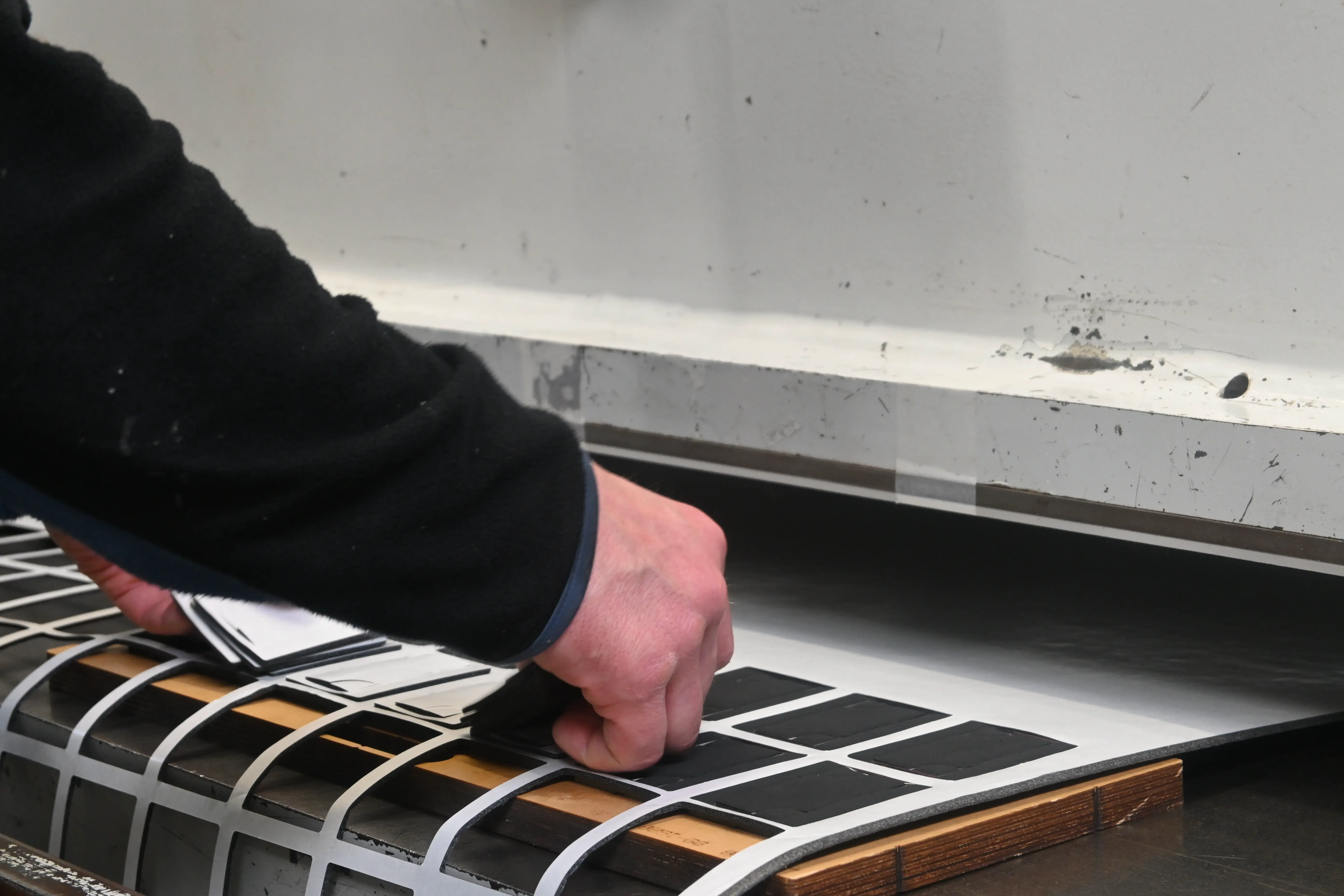 Hand einer Person, die Papier auf einem Stapelhalter oder Drucker in einer Arbeitsumgebung ausrichtet oder handhabt.