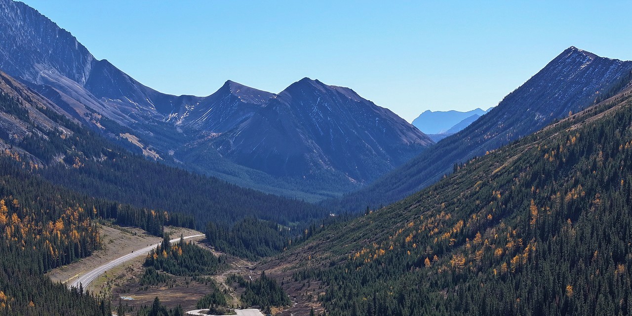 Highway 40 winding through Highwood Pass in Peter Lougheed Provincial Park with autumn golden larches on mountain slopes and dramatic Rocky Mountain peaks