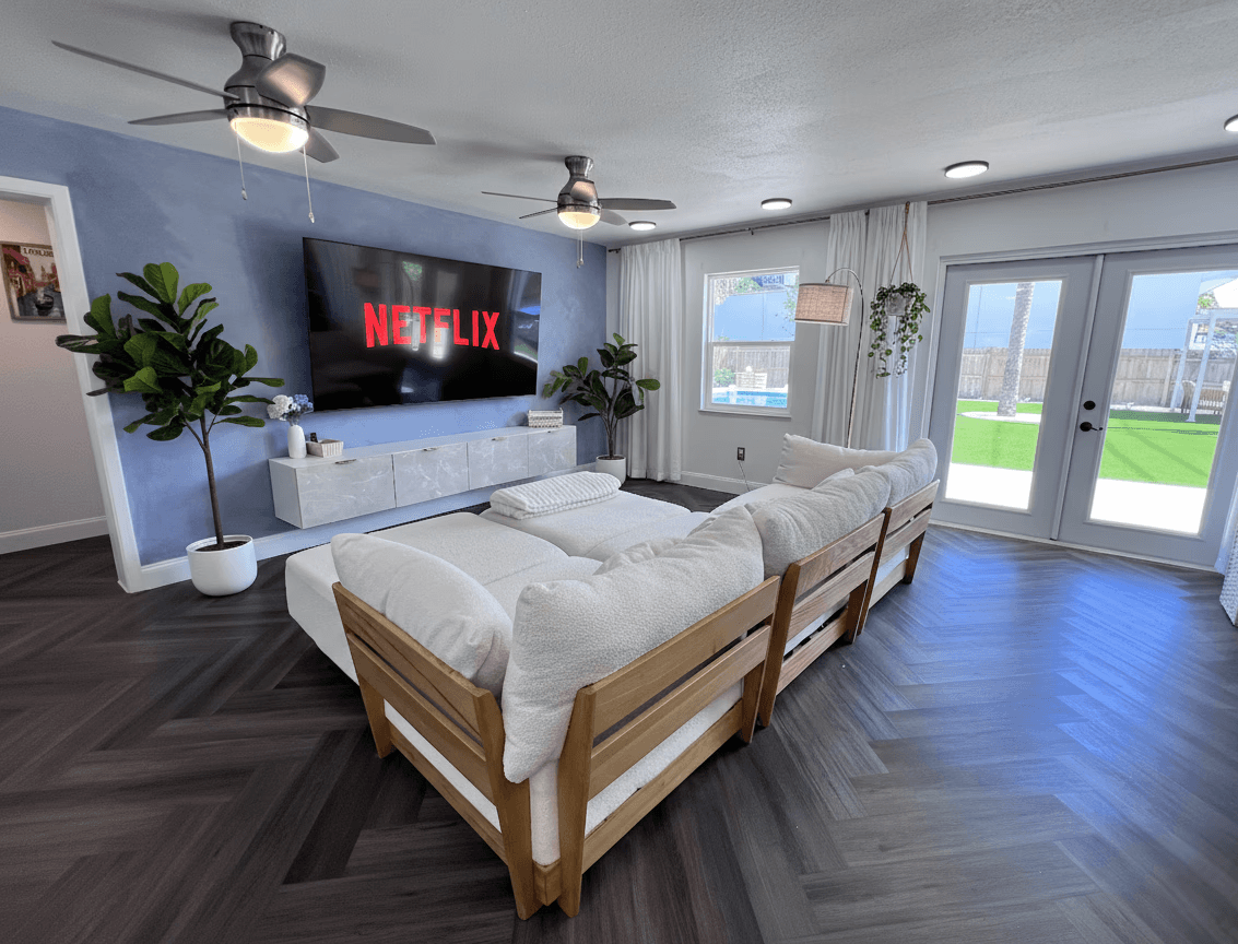 Beautiful sunlit living room with elegant French doors, plush sectional & Cinema style 85” Smart TV, the ultimate movie night retreat