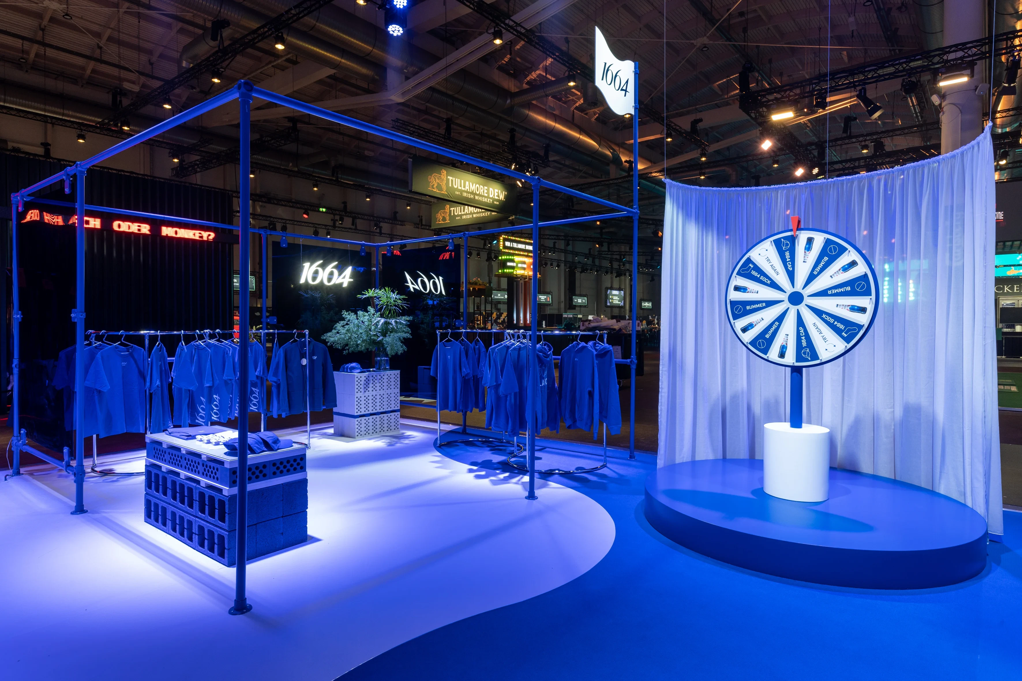 Merchandise area of the 1664 Blanc booth with blue shirts on racks, crate displays and a blue-white wheel of fortune.