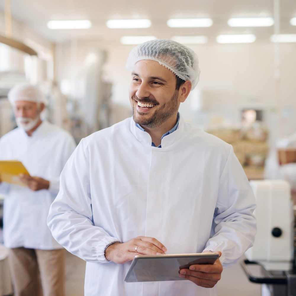 A person wearing hair net and chefs uniform carrying a clipboard