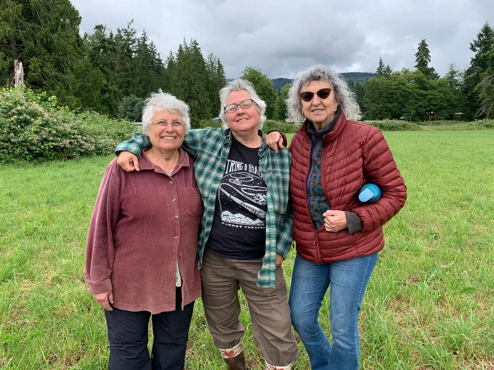 Three woman standing next too each other on open land.