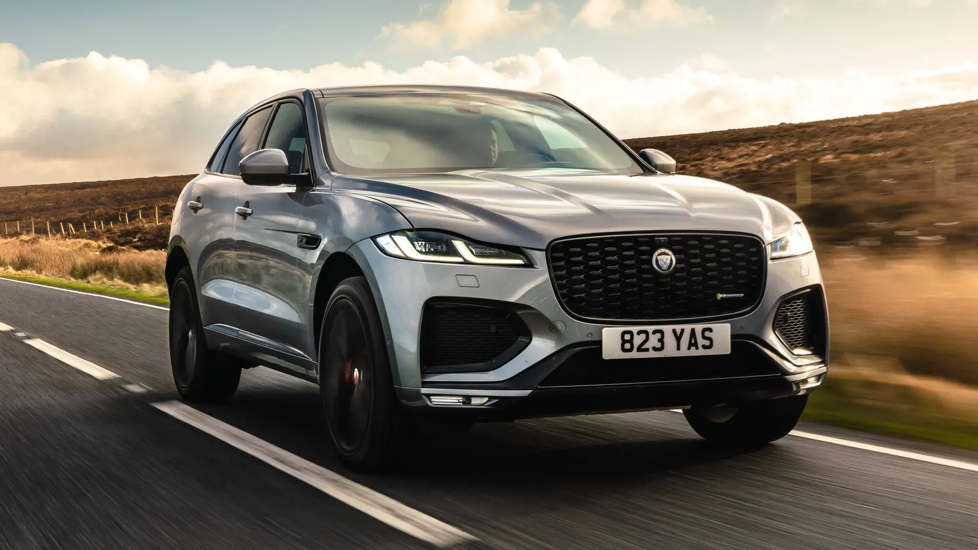 Silver luxury SUV driving on a paved road through a grassy landscape