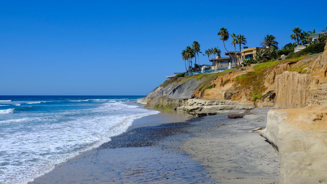 Modern glass and wood cabin with a cozy outdoor deck featuring wicker furniture, surrounded by lush green trees and a serene forest setting.