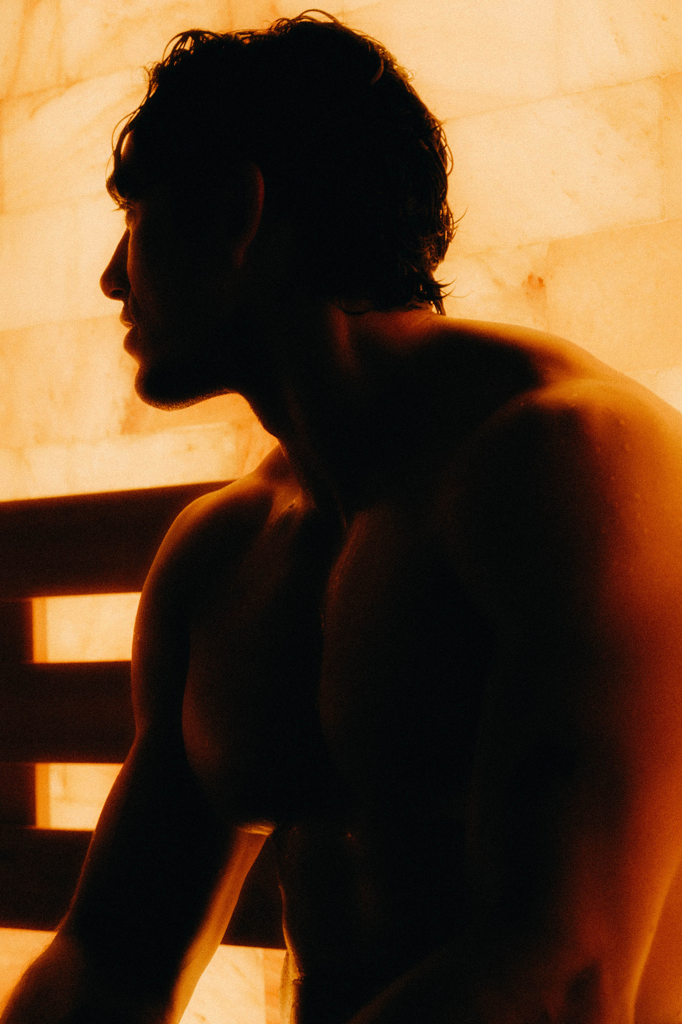 Profile silhouette of a person sitting quietly inside a warmly lit sauna, settling into the heat