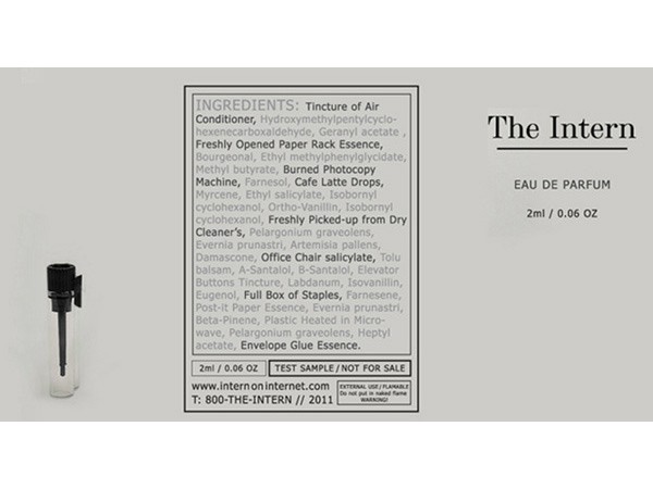 A small vial labeled “The Intern” is displayed alongside a printed list of ingredients: Tincture of Air, Conditioner, Hydroxymethylpentylcyclohexenecarboxaldehyde, Geranyl acetate, Freshly Opened Paper Rack Essence, Bourgeoisol, Ethyl methylphenylglycidate, Methyl butyrate, Burned Photocopy Machine, Farnesol, Cafe Latte Drops, Myrcene, Ethyl salicylate, Isobornyl cyclohexanol, Ortho-Vanillin, Isobornyl cyclohexanone, Freshly Picked-up from Dry Cleaner’s, Pelargonium graveolens, Evernia prunastri, Artemisia pallens, Evernia prunastri, Artemisia pallens, Balsam, A-Santalol, B-Santalol, Elevator Buttons Tincture, Labdanum, Isovanillin, Eugenol, Full Box of Staples, Farnesene, Post-It Paper Essence, Evernia prunastri, Beta-Pineene, Plastic Heated in Micro-wave, Pelargonium graveolens, Heptyl acetate, Envelope Glue Essence. The label also includes “2ml / 0.06 OZ” and “TEST SAMPLE / NOT FOR SALE,” along with the website www.intern.on.intern.com and phone number 800-THE-INTERN.