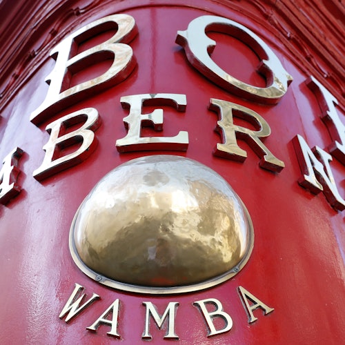 紅色牆面特寫,上面有金屬字母「BOI」、「BER」和「WAMBA」,圍繞著一個光滑、突出的金色圓頂。