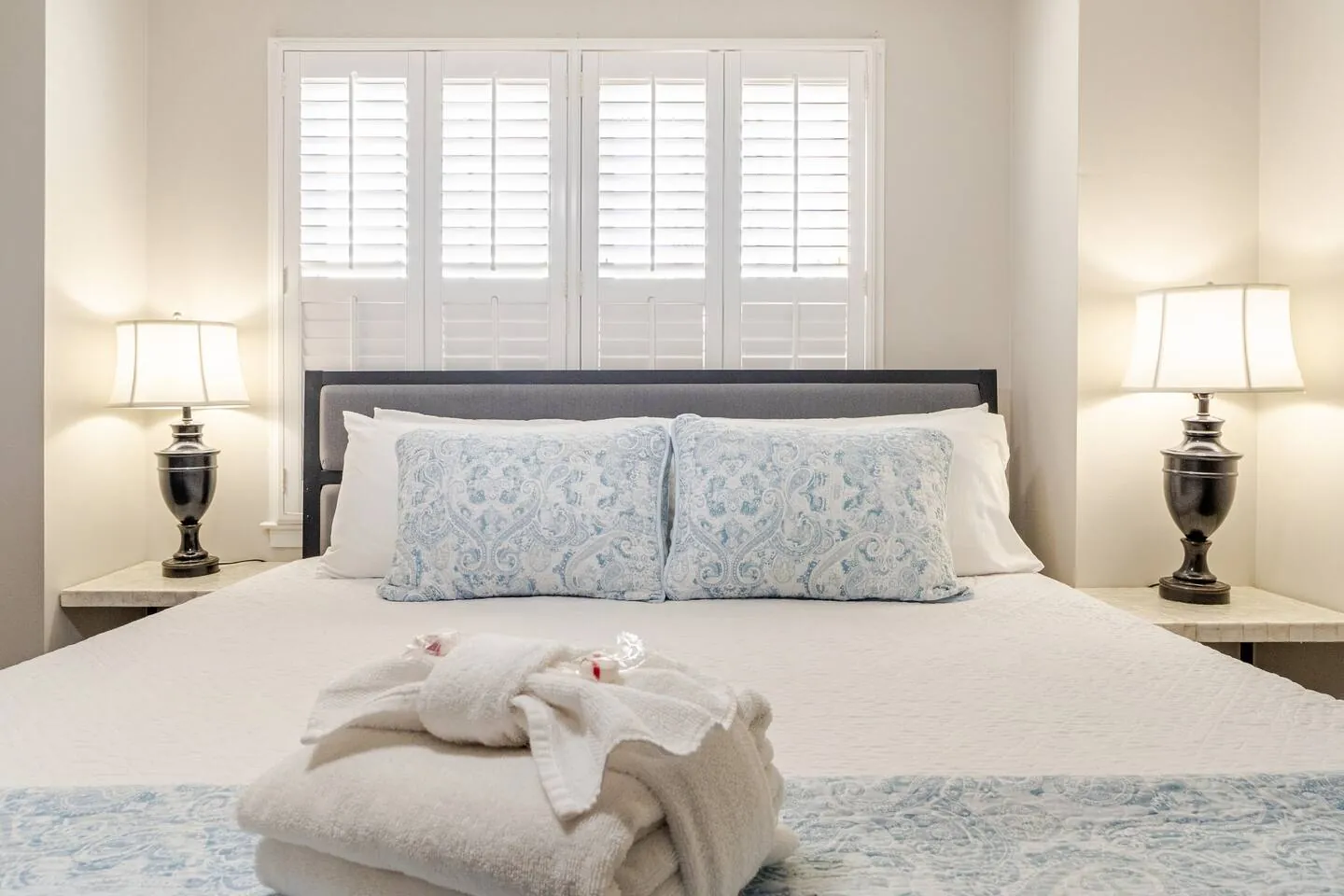 King bed with blue pillows under white plantation shutters