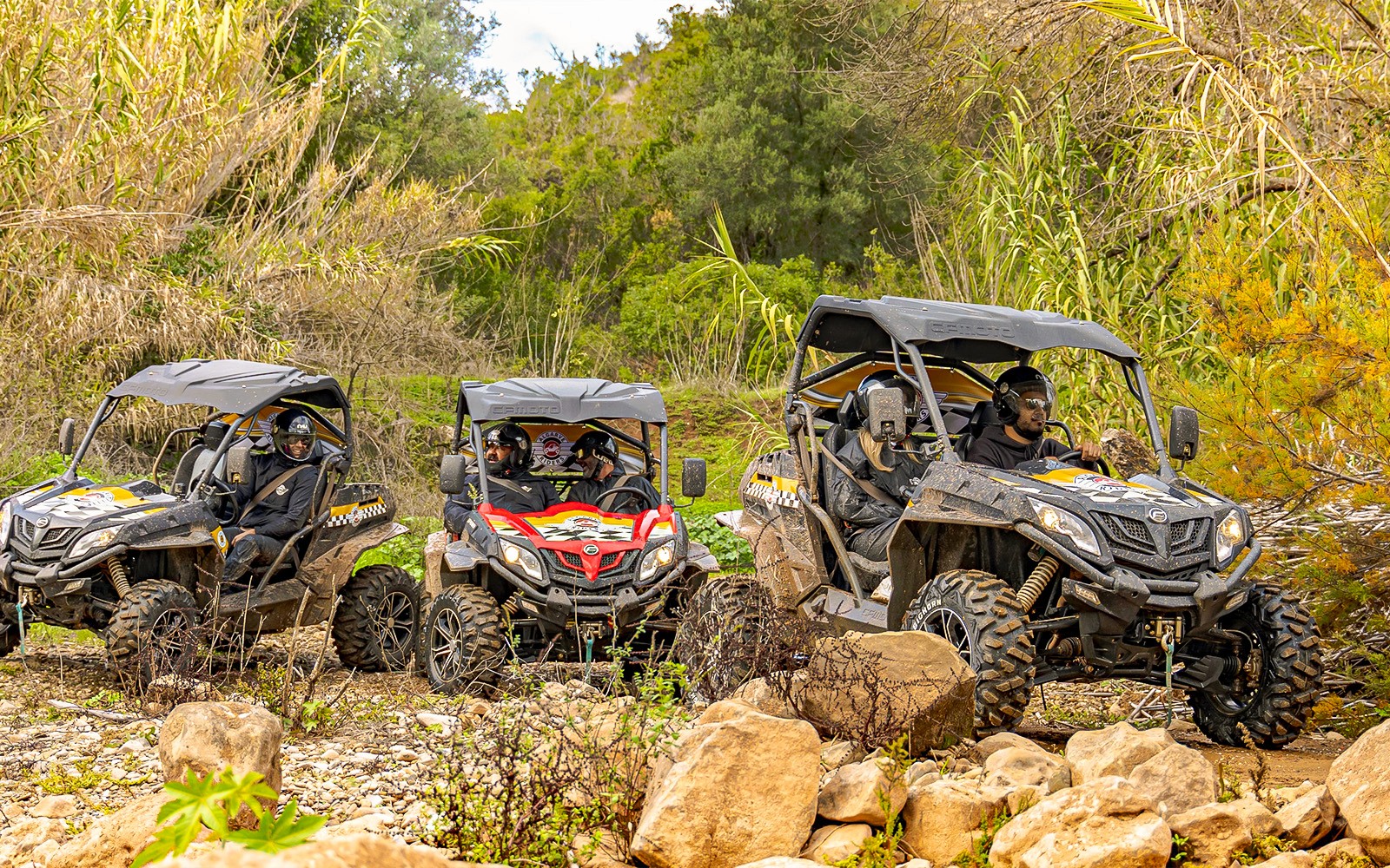 Passeio de buggy por terreno rochoso no Algarve, Portugal, com vegetação exuberante ao fundo.