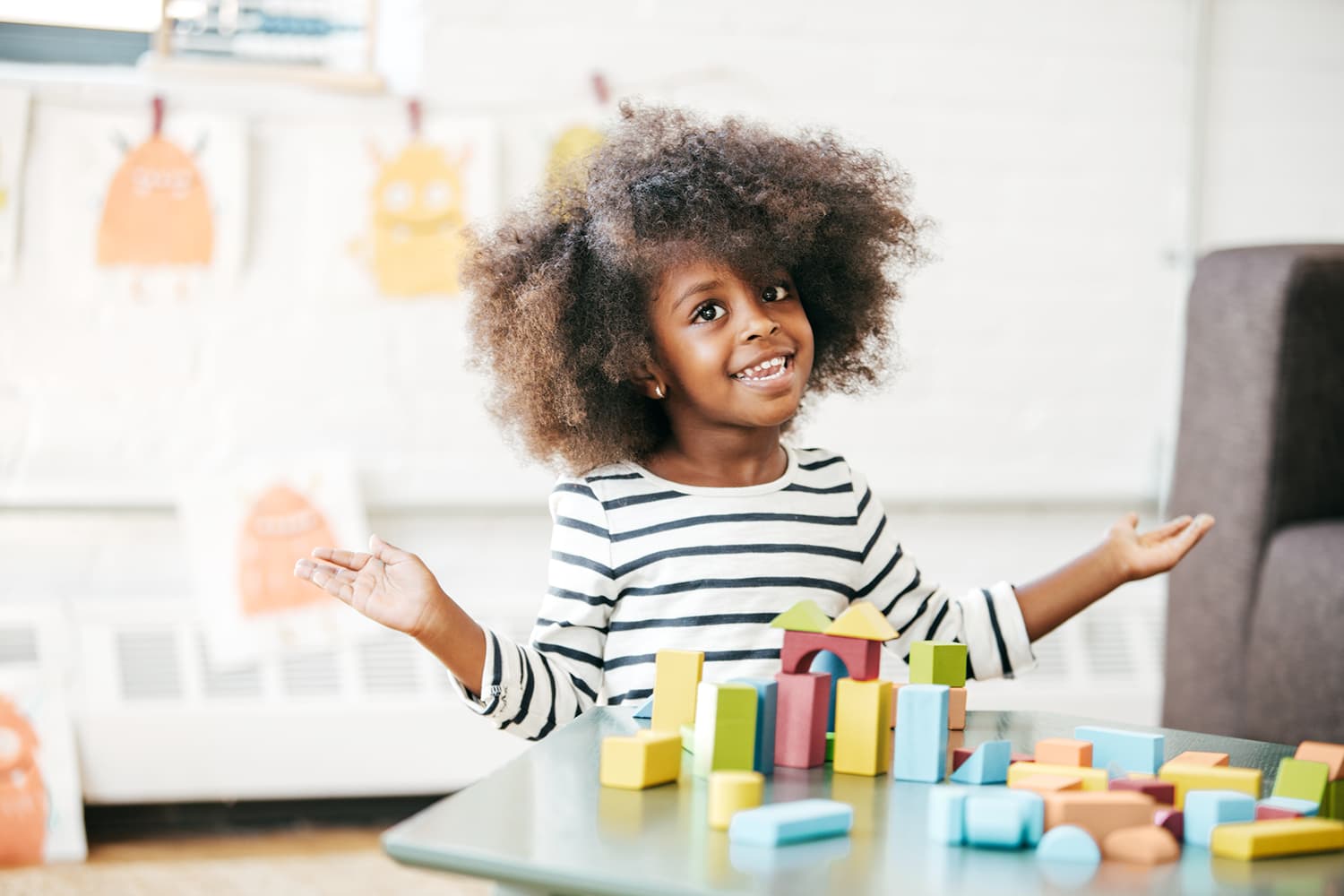 Young 6 year old girl, smiling while playing with colorful blocks during a speech therapy session in a bright, child-friendly space.