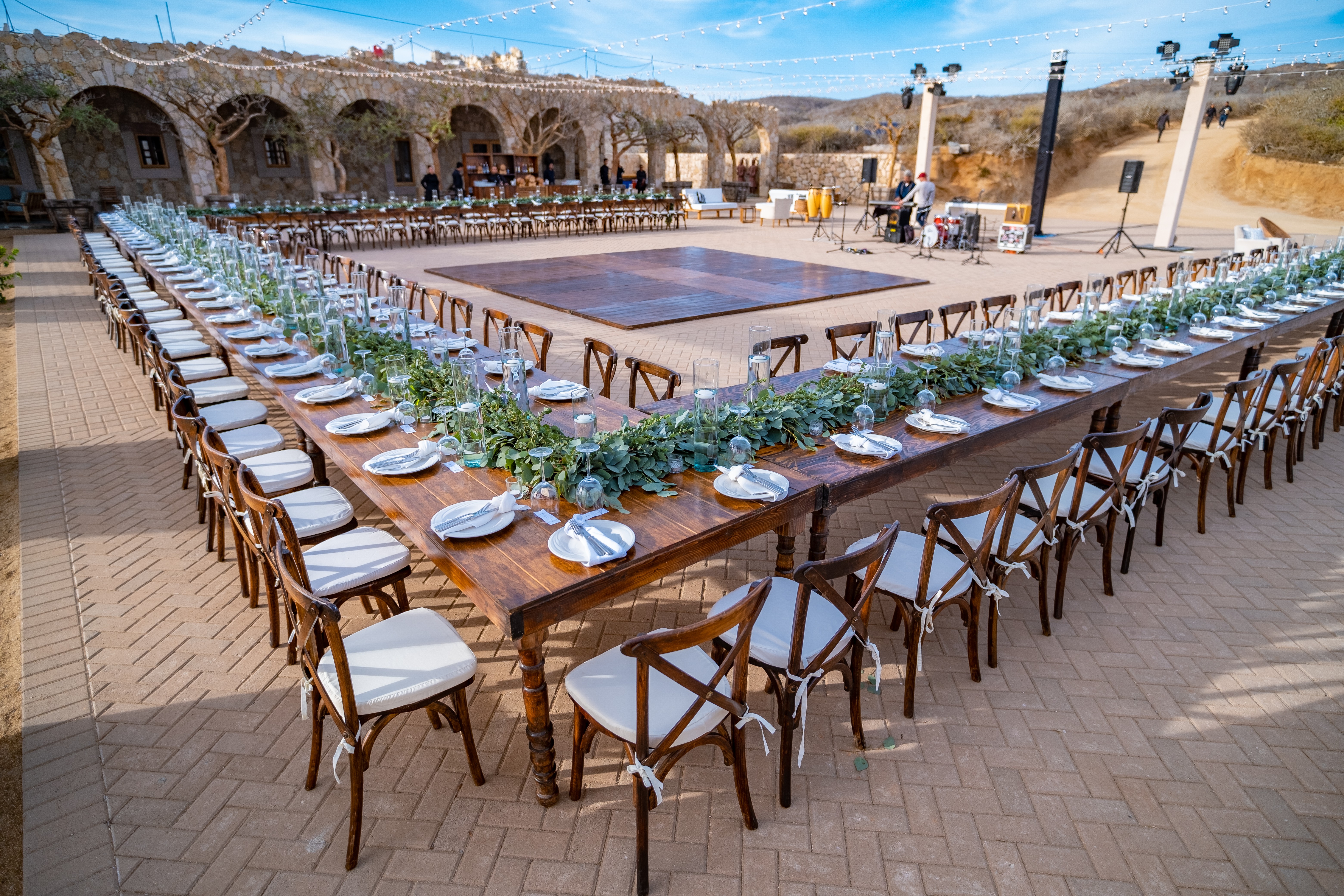 Beautiful beach wedding ceremony with a couple standing under an archway adorned with flowers, white chairs line the sandy aisle.