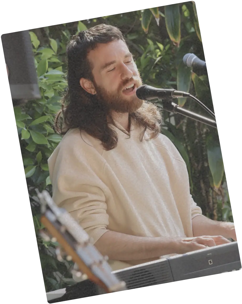 Person singing outdoors at a microphone with eyes closed in a hoodie.