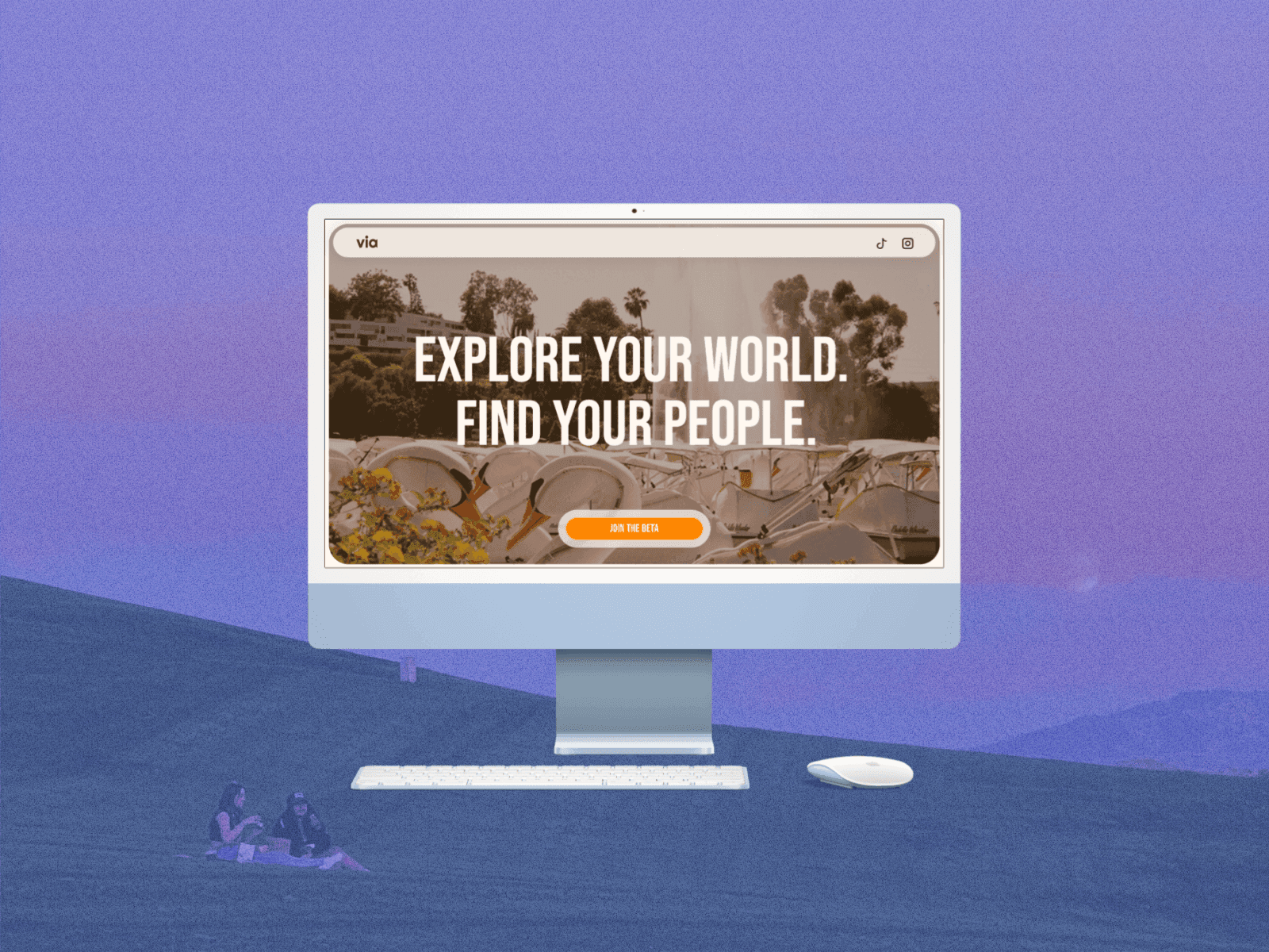A desktop computer with a keyboard and mouse with the screen open to the via homepage. The computer is superimposed on a faded image of two young women having a picnic on a grassy hill at sunset