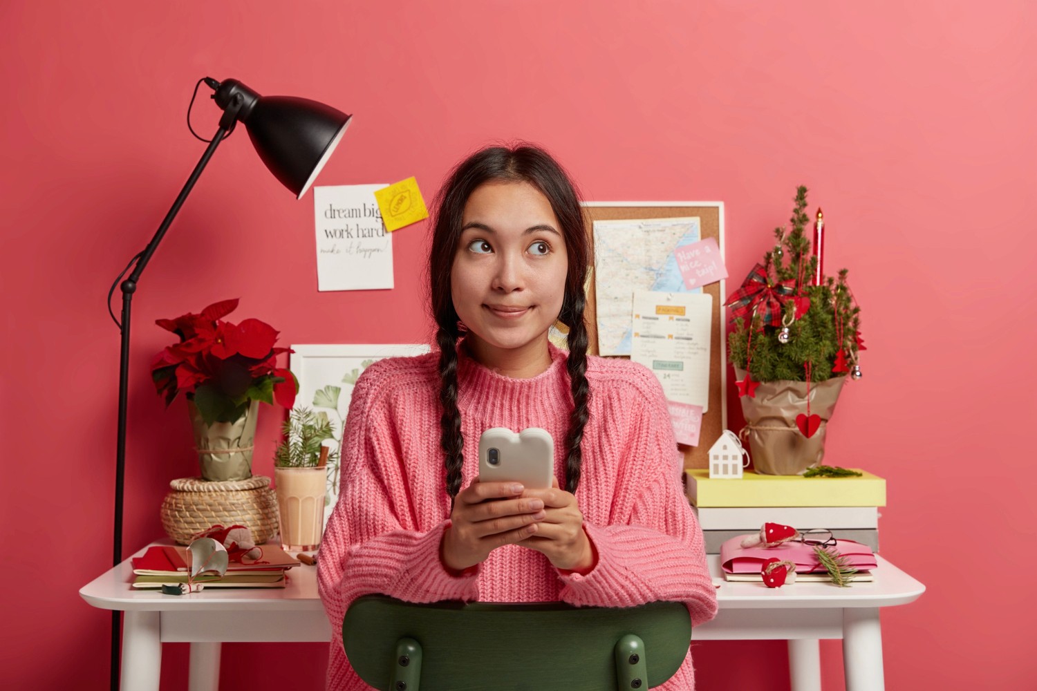 A girl wearing a pink sweater is holding a cell phone, smiling as she engages with the device.