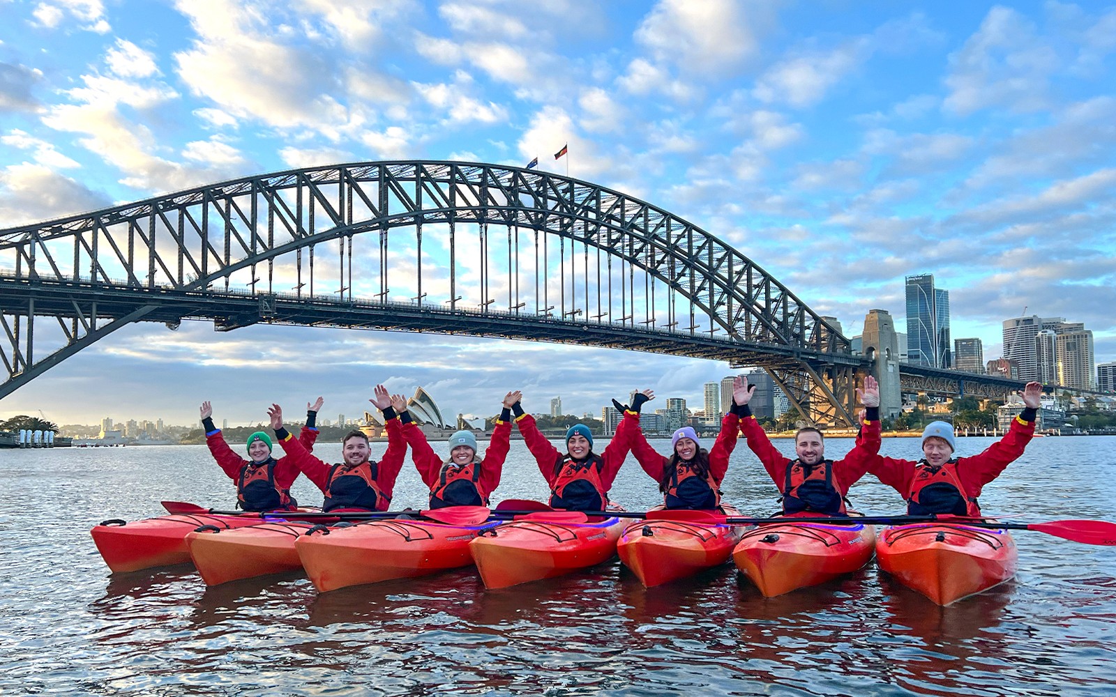 一群人在悉尼港享受皮划艇之旅，背景是著名的悉尼歌剧院，提供可選早餐服務