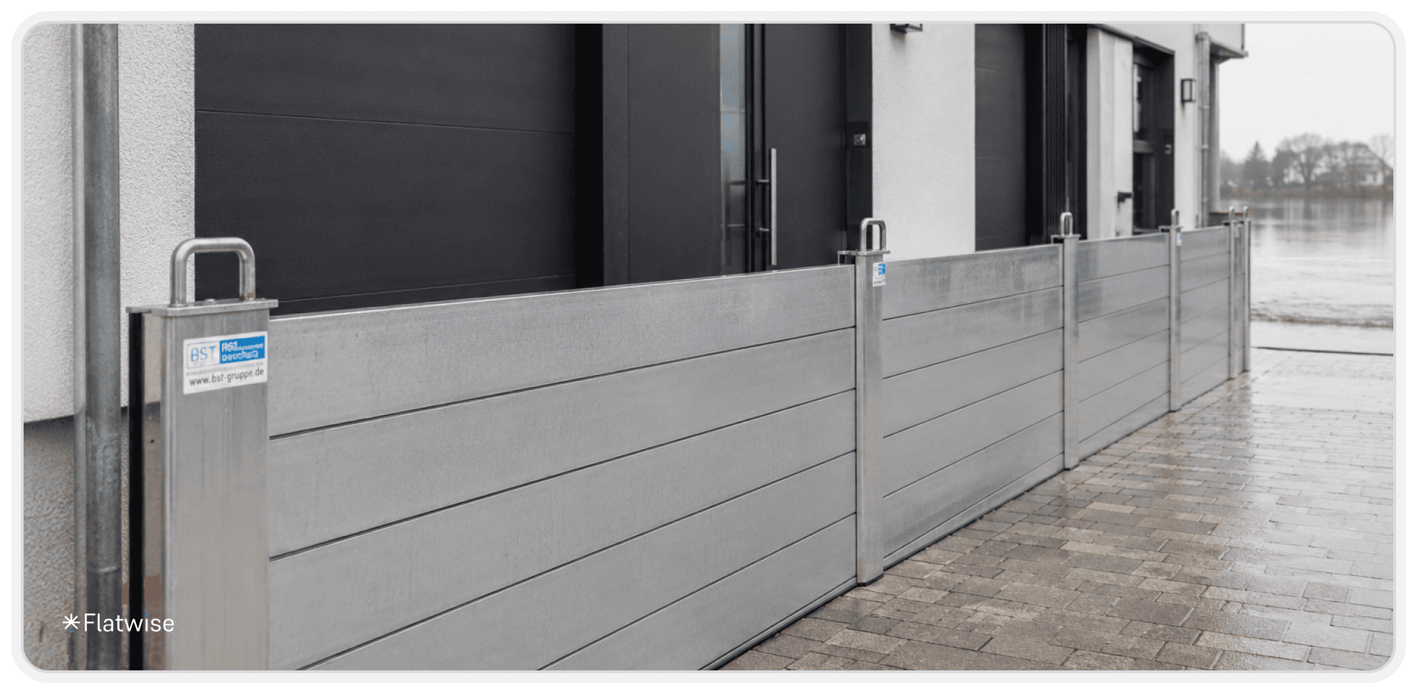 Moderner Hochwasserschutz aus Aluminiumplatten vor den Eingängen eines Wohngebäudes. Die Schutzbarrieren sind entlang der Gebäudefassade montiert und dienen dem Schutz vor eindringendem Hochwasser.