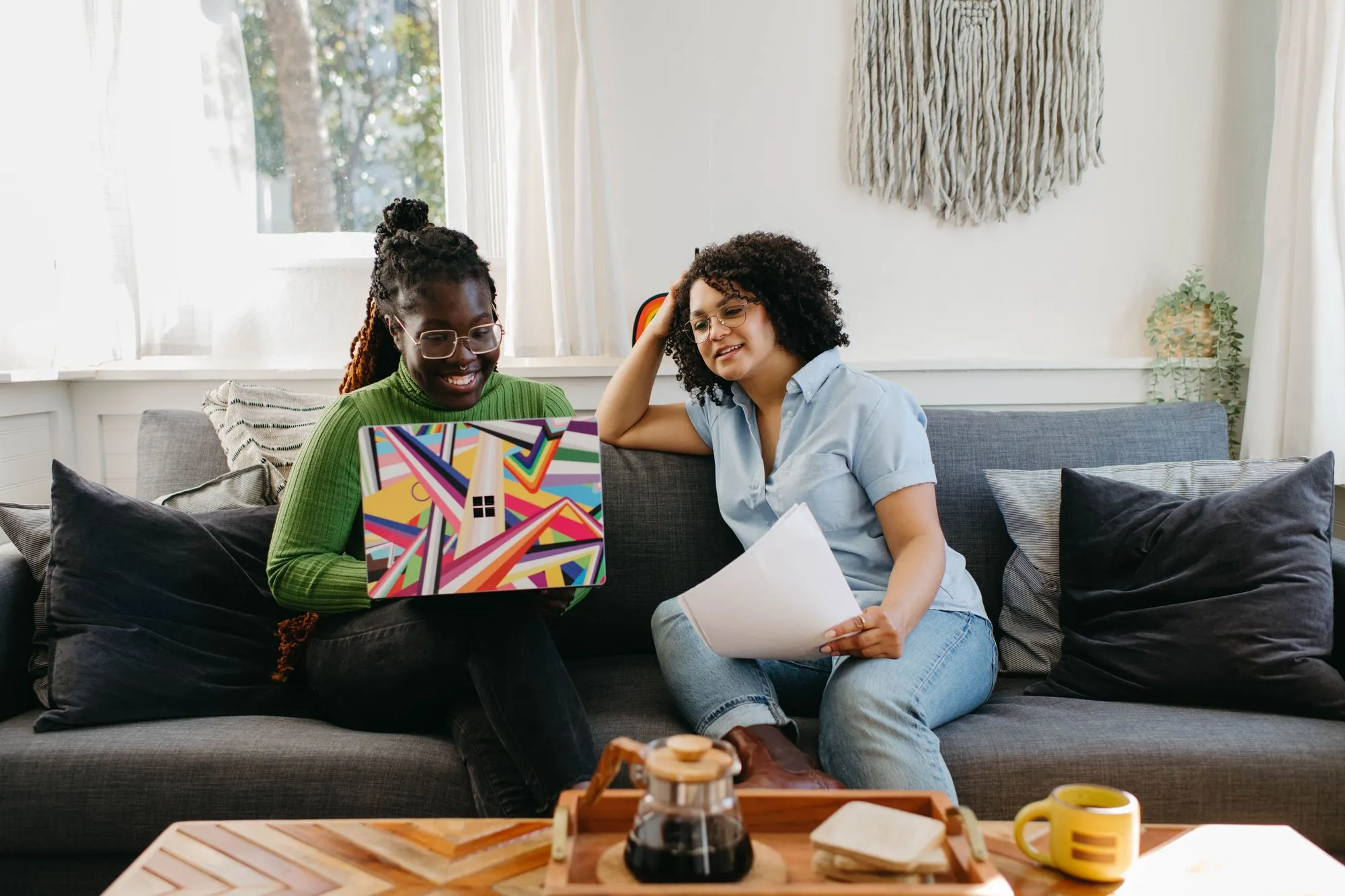 Two women chatting on a couch while looking at a laptop