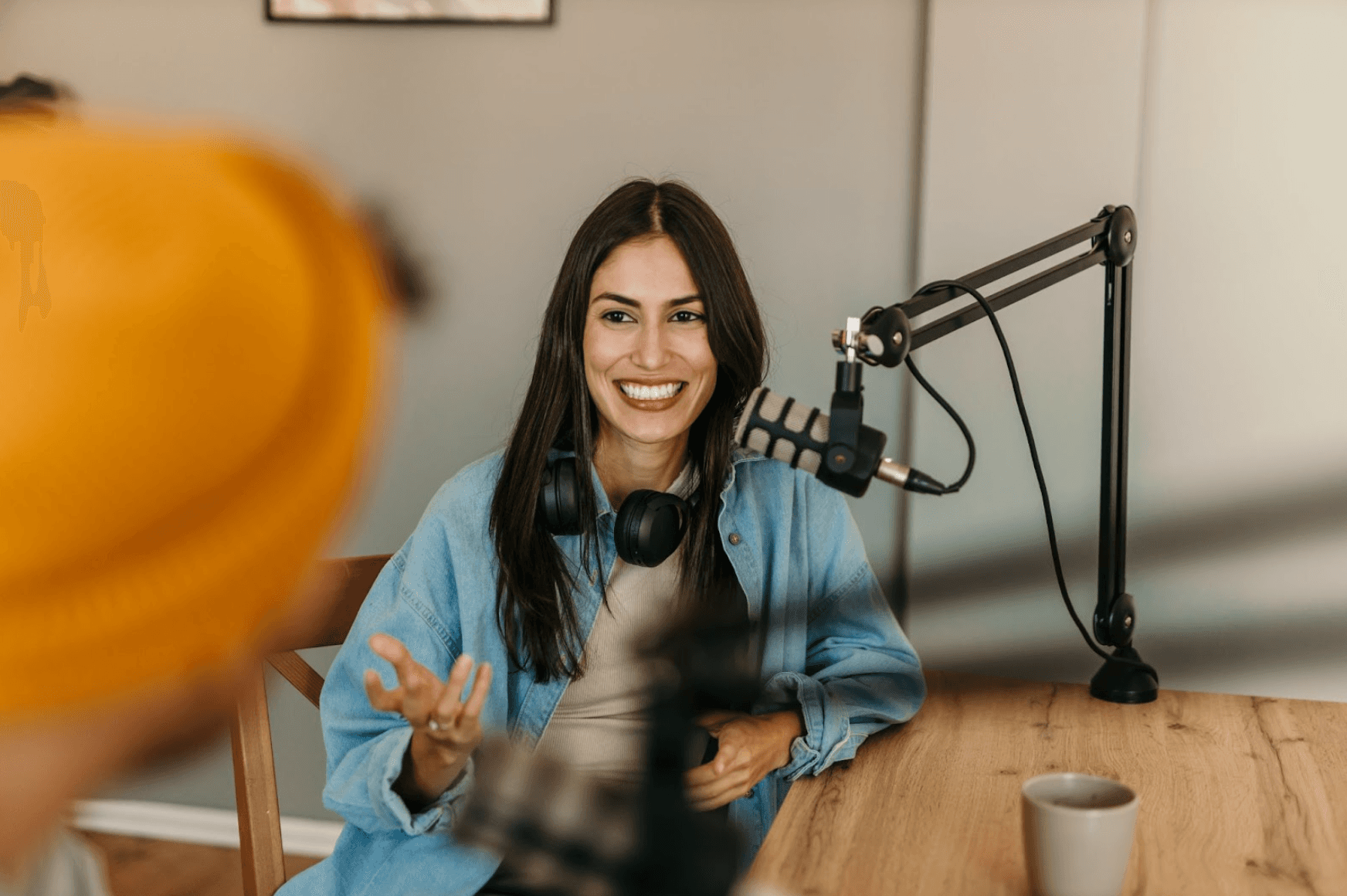 Smiling woman seated at a podcast setup with a microphone and headphones—representing content creation or digital media production.