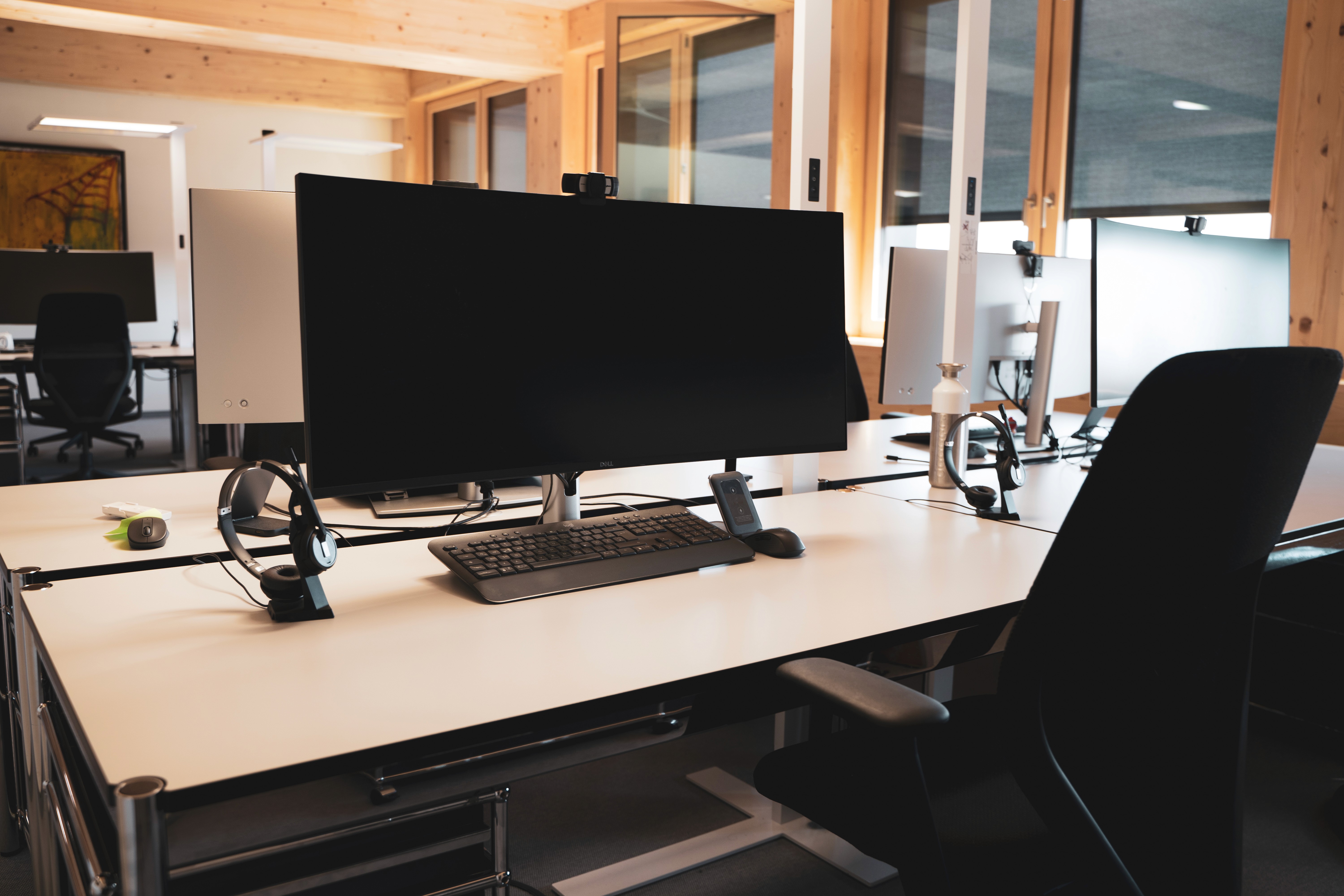 Moderner Arbeitsplatz mit Schreibtisch, ergonomischem Stuhl und großem Bildschirm in heller Umgebung. Steht für produktives Arbeiten und technologische Ausstattung.