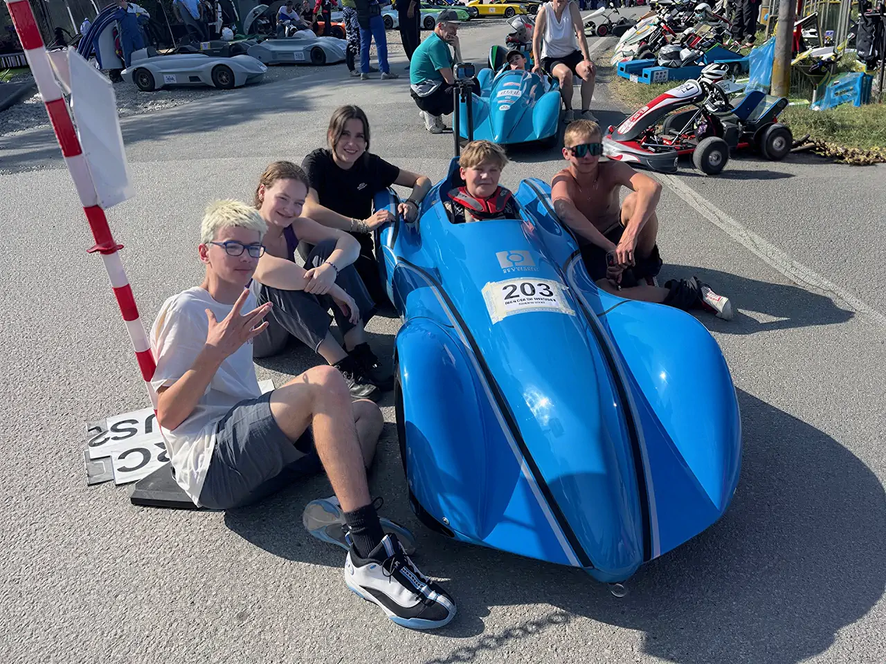 Groupe de jeunes pilotes posant autour d'une caisse à savon bleue lors d'une compétition européenne de speed down