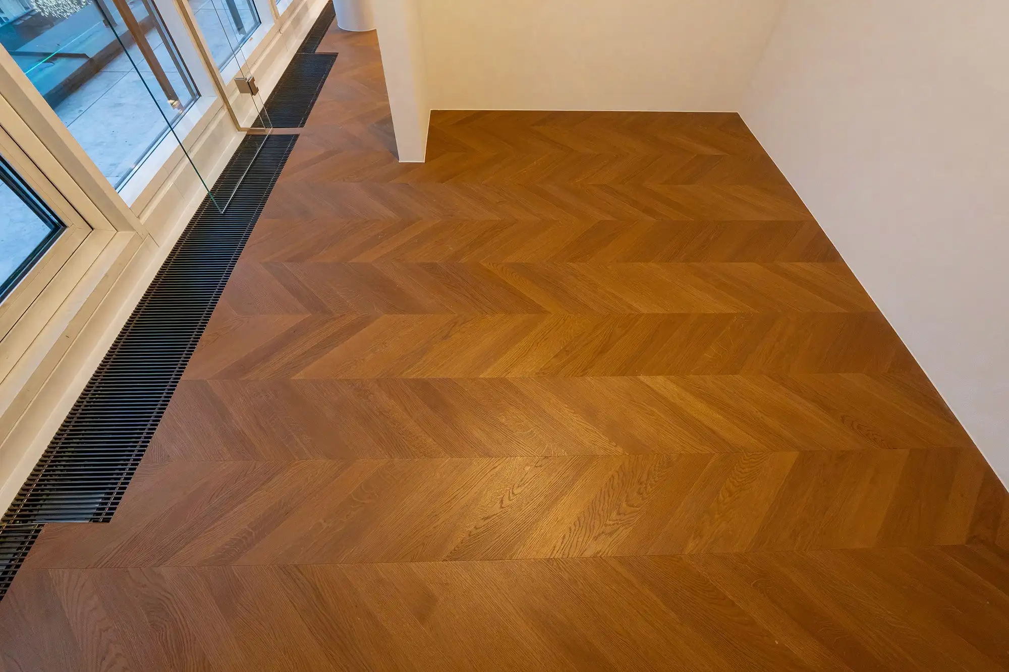 Heller Raum mit stilvollem Chevron-Parkettboden und bodentiefem Fensterbereich.