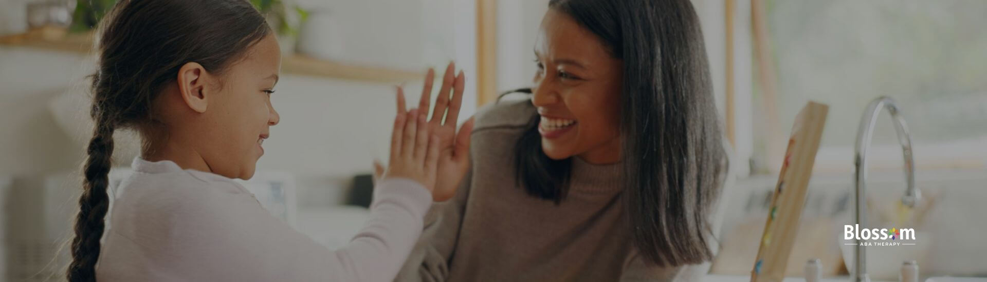 A girl with autism high-fiving her ABA therapist while smiling during an ABA therapy session at home.