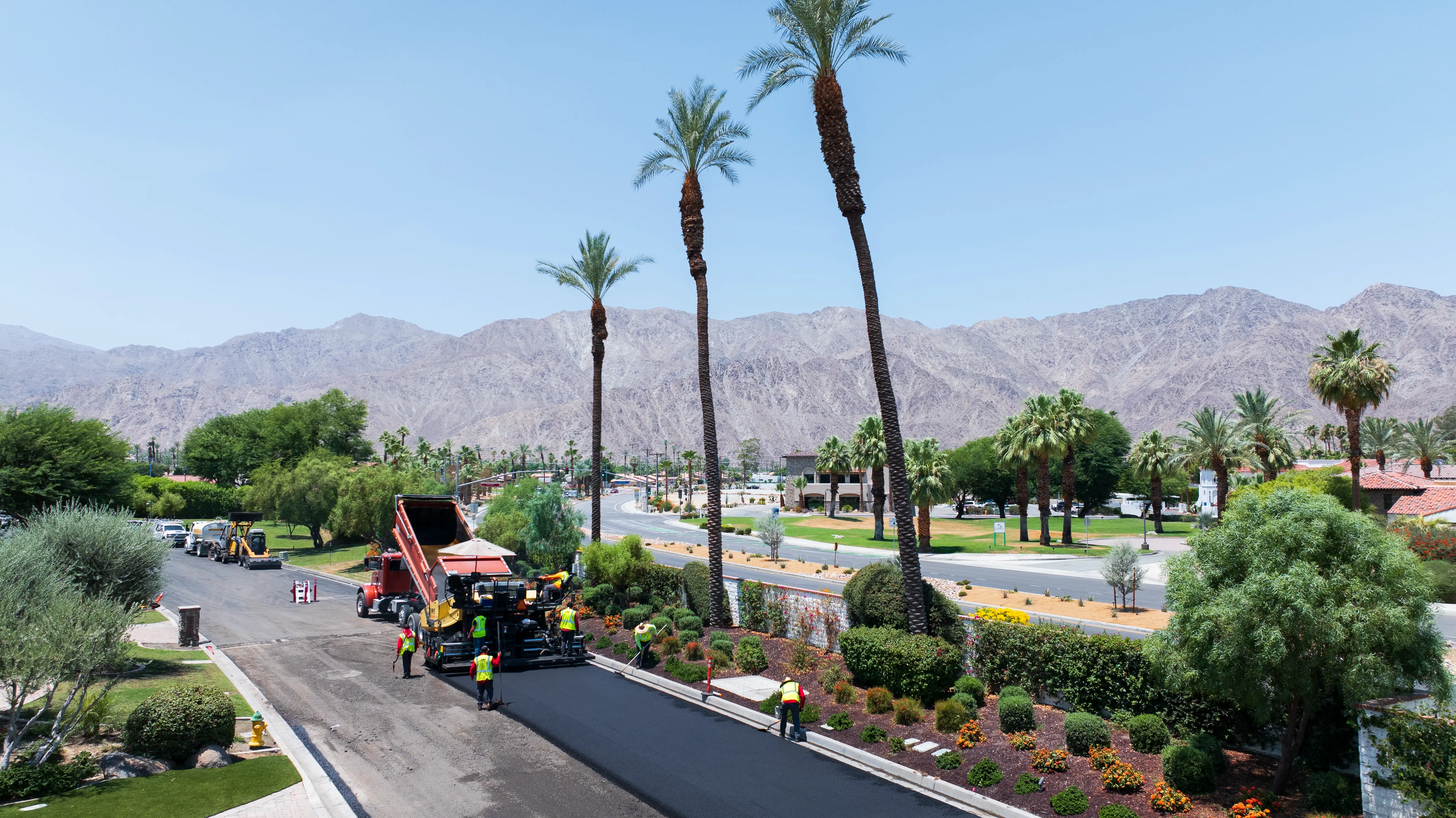 Paving machine laying hot asphalt on private street with palm trees