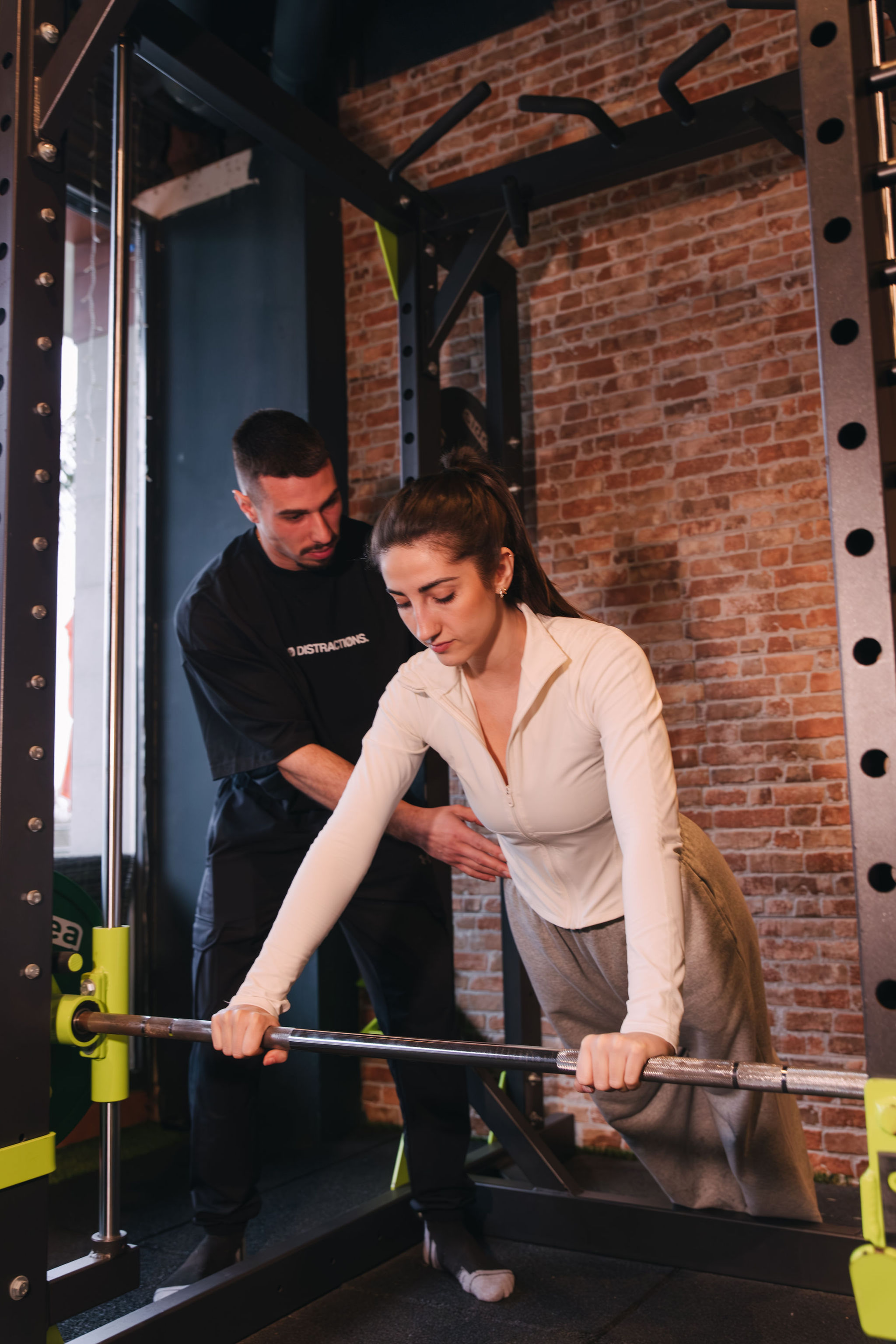 Entrenadora corrigiendo técnica de flexión inclinada a clienta en La Base Strength, Sitges