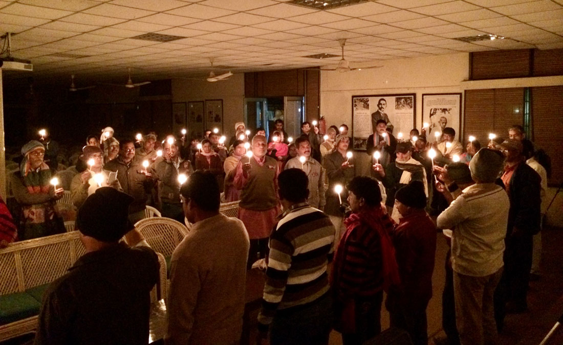 Smiling young man with short hair poses against a dark background, wearing a green button-up shirt.
