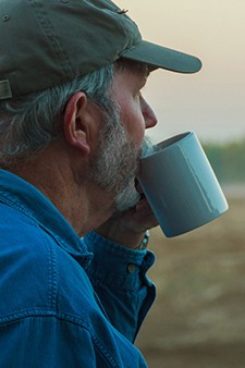Bonde som drikker kaffe og ser utover på jordet