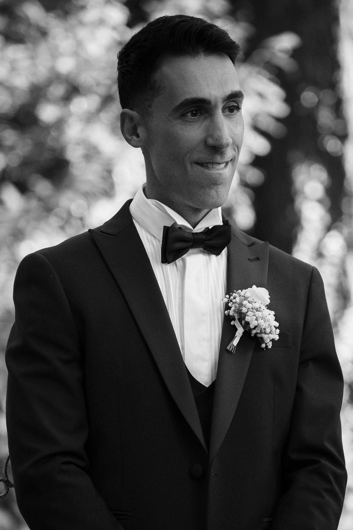 Fabio in smoking con fiocco e boutonnière bianca sorride in giardino, ritratto dello sposo a Villa Ferrari