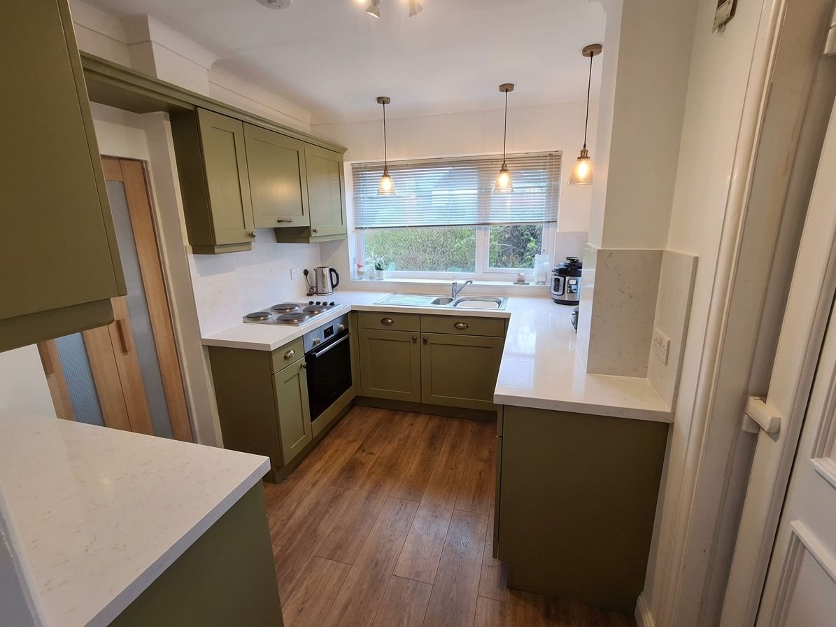 Olive green kitchen cabinets with warm wood floor and bronze hardware