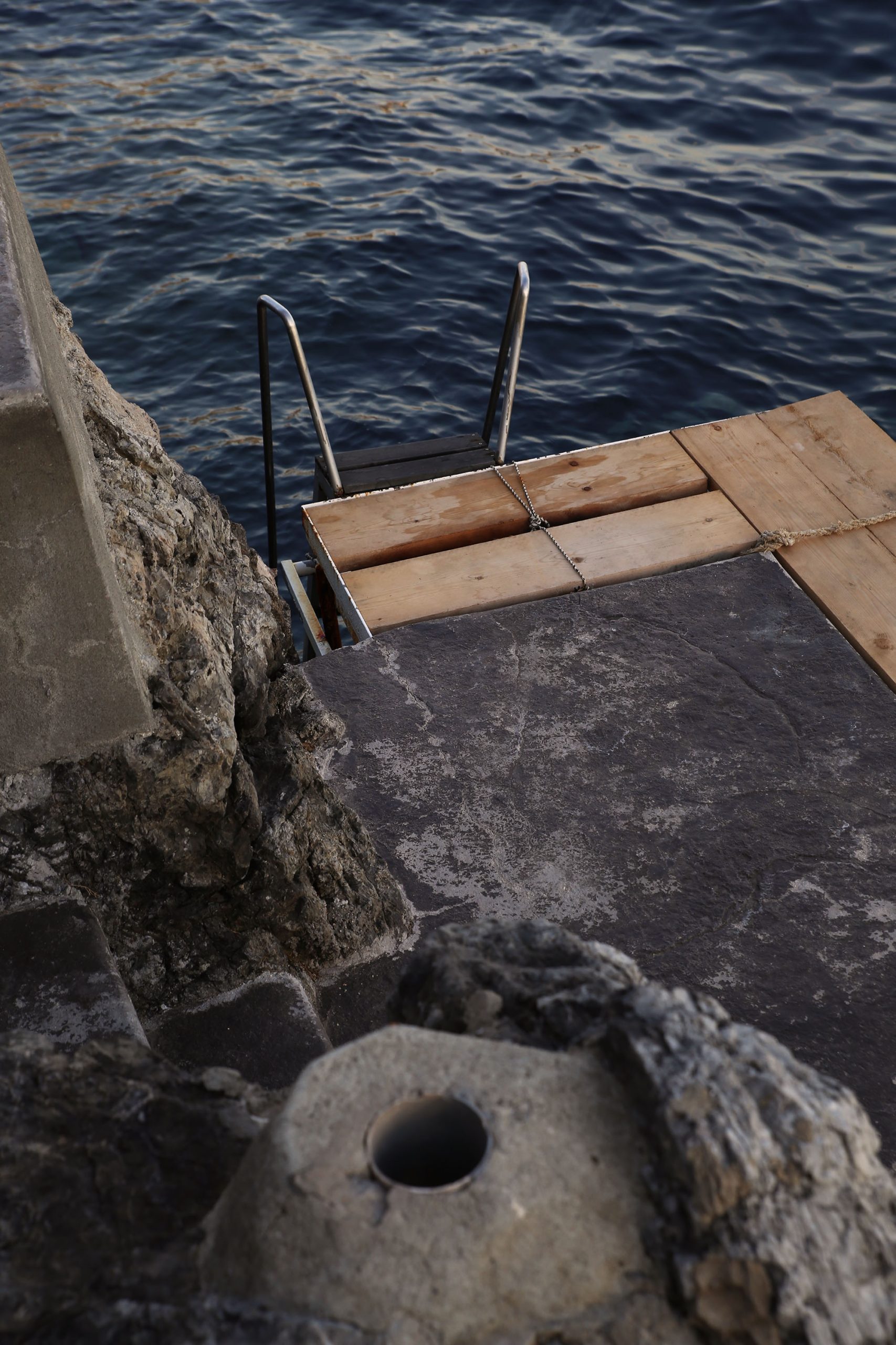 Metal ladder leading down to the sea from a rocky, wood-planked jetty