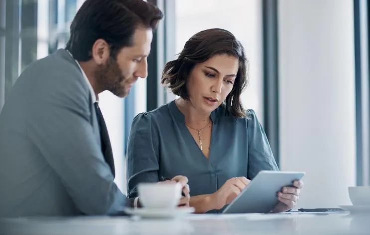 Business professionals reviewing a tablet to discuss financial strategies for debt relief and wealth building.