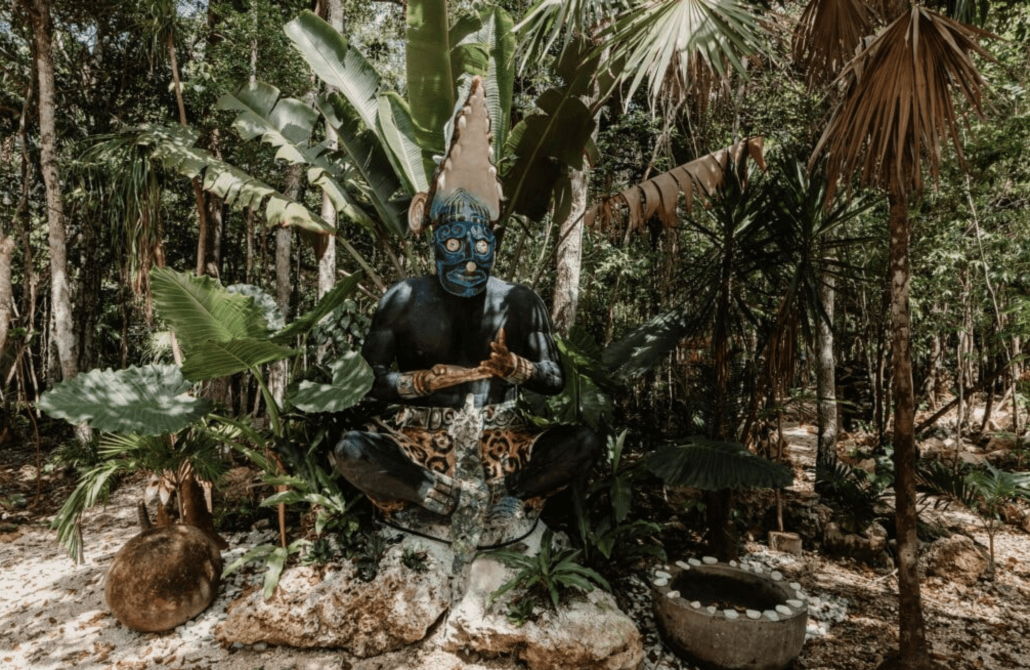 A group of six people gather around a wooden table where an older man in an apron kneads dough