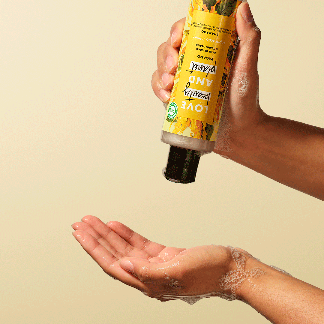 A hand holds a yellow bottle above an open palm, ready to dispense its contents against a light background.