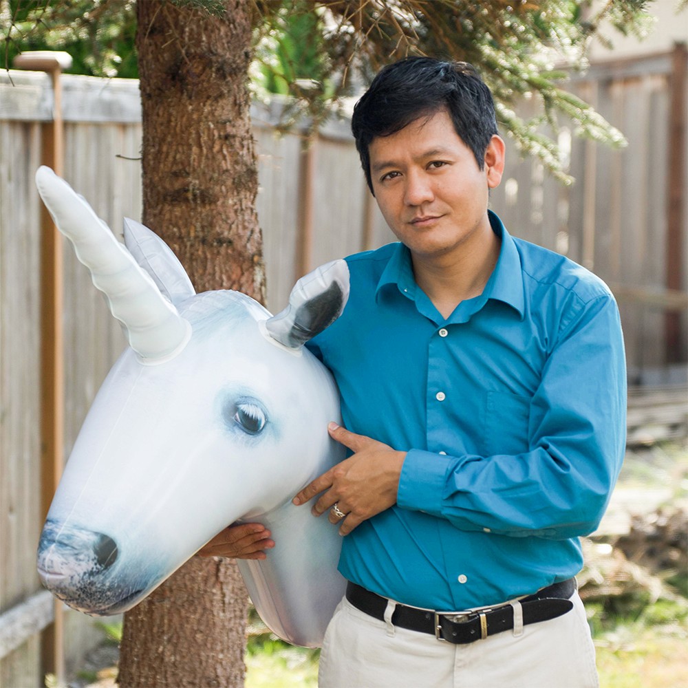 A portrait of Vu Le holding an inflatable unicorn