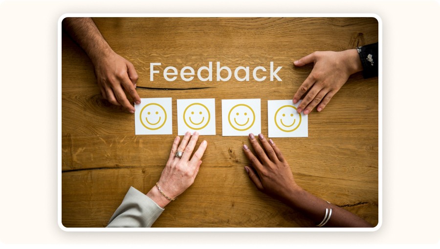 Hands placing smiley cards under “Feedback” text on wooden table
