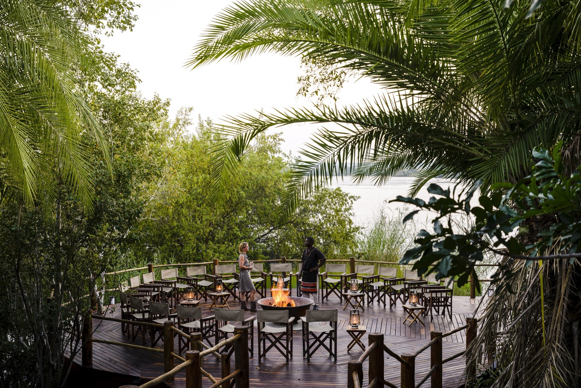 A firelit deck gathering beside the river at dusk