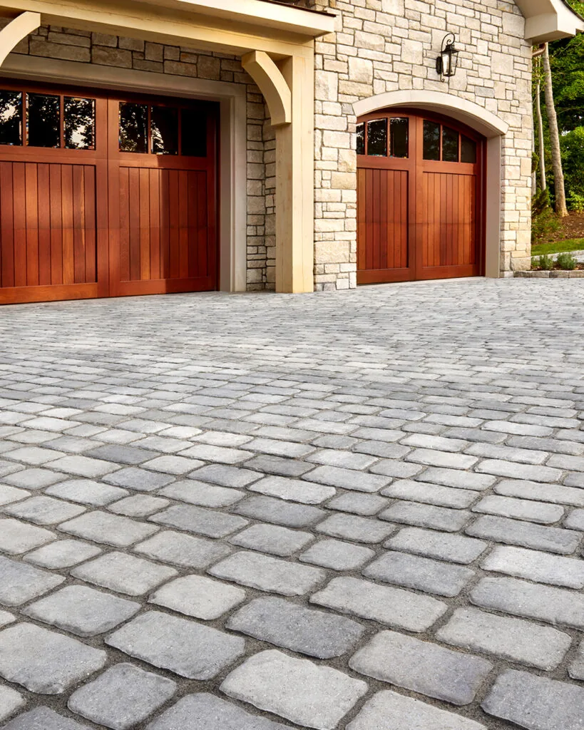 Gray paver driveway leading to wood garage doors on a stone-faced home.