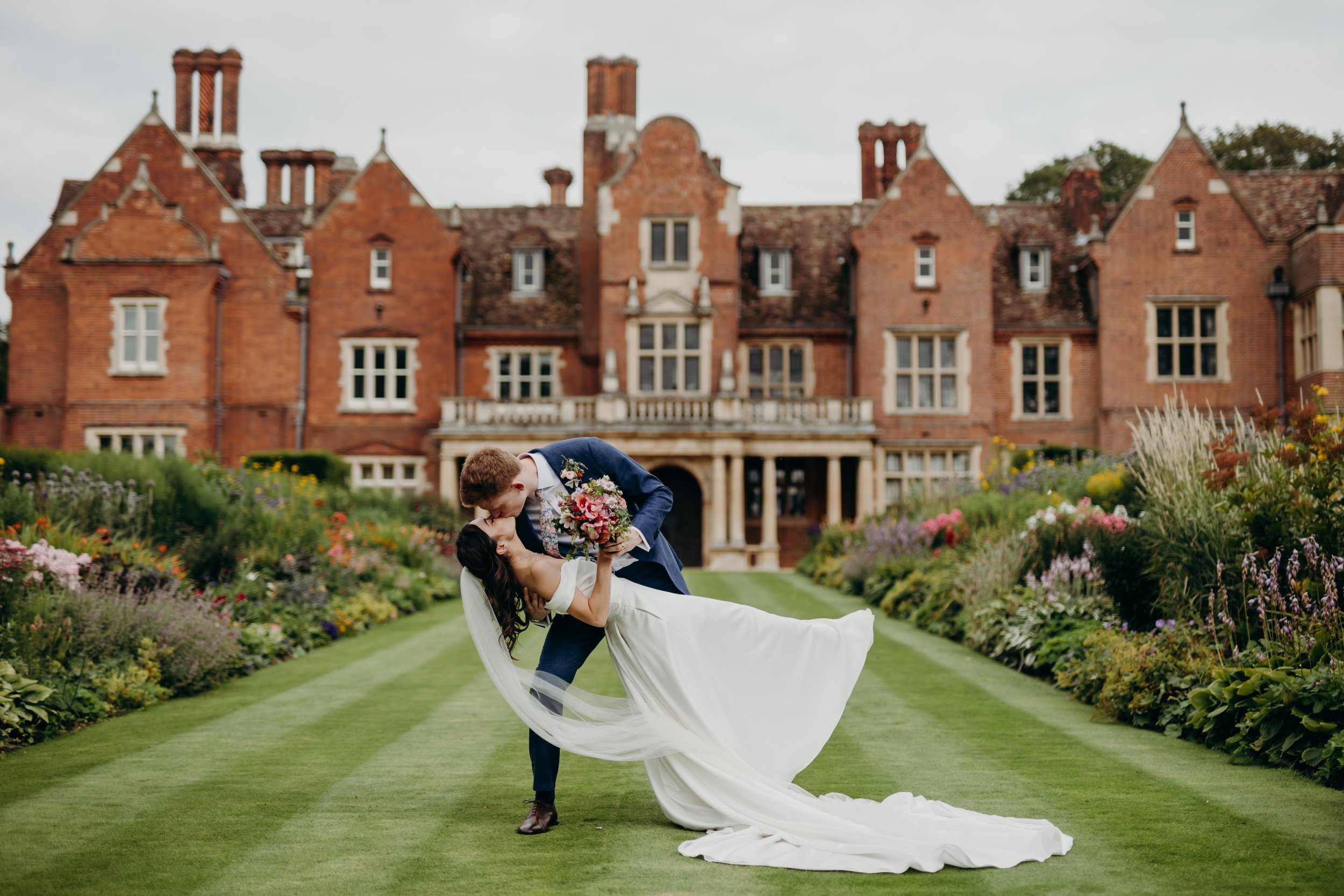 Married couple kissing infront of a manor house on the lawn