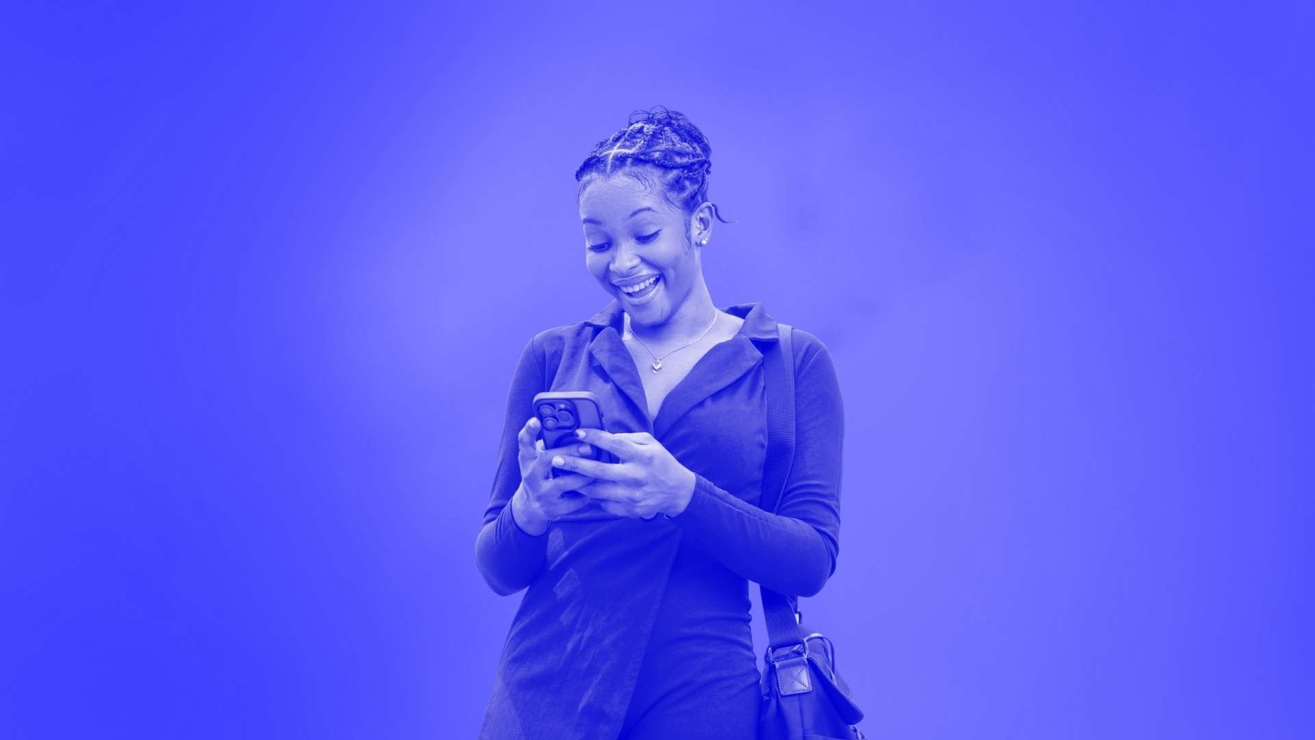 A woman with her hair tied back looking at the phone she is holding and wearing a satchel over her shoulder