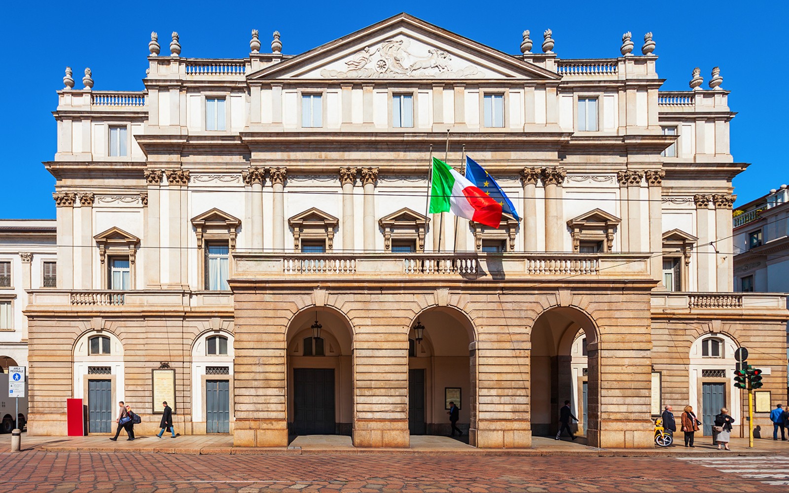 La Scala opera house facade in Milan with Italian and EU flags.