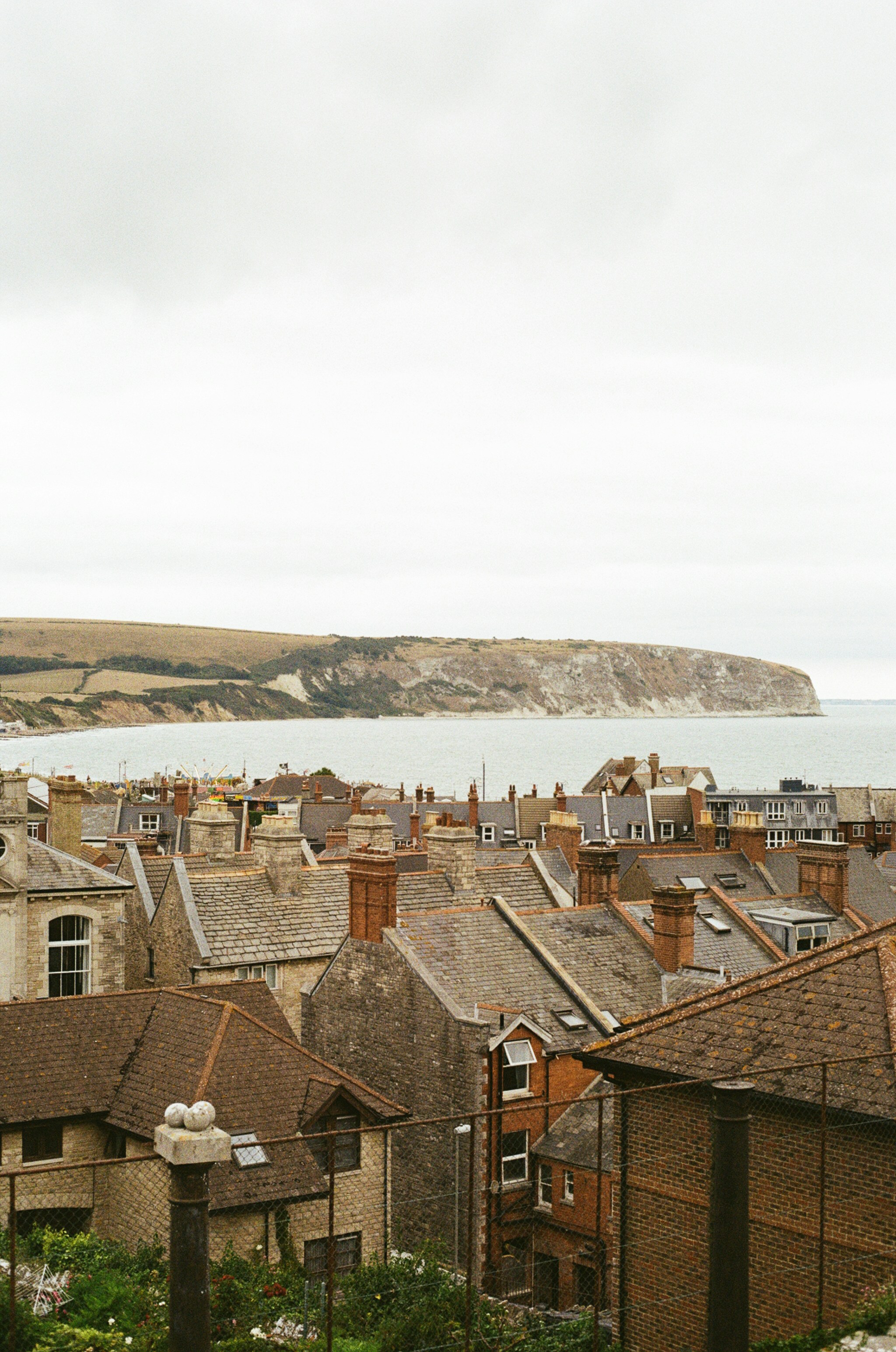 Rooftops of a coastal town with a distant cliff.