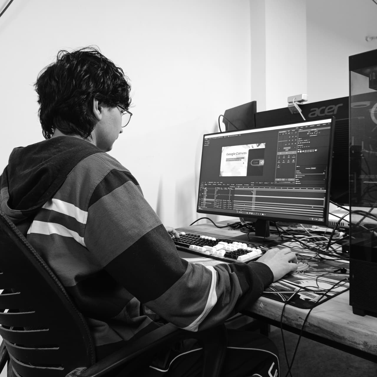 Black and white photo of two people looking at a computer screen with papers on wall