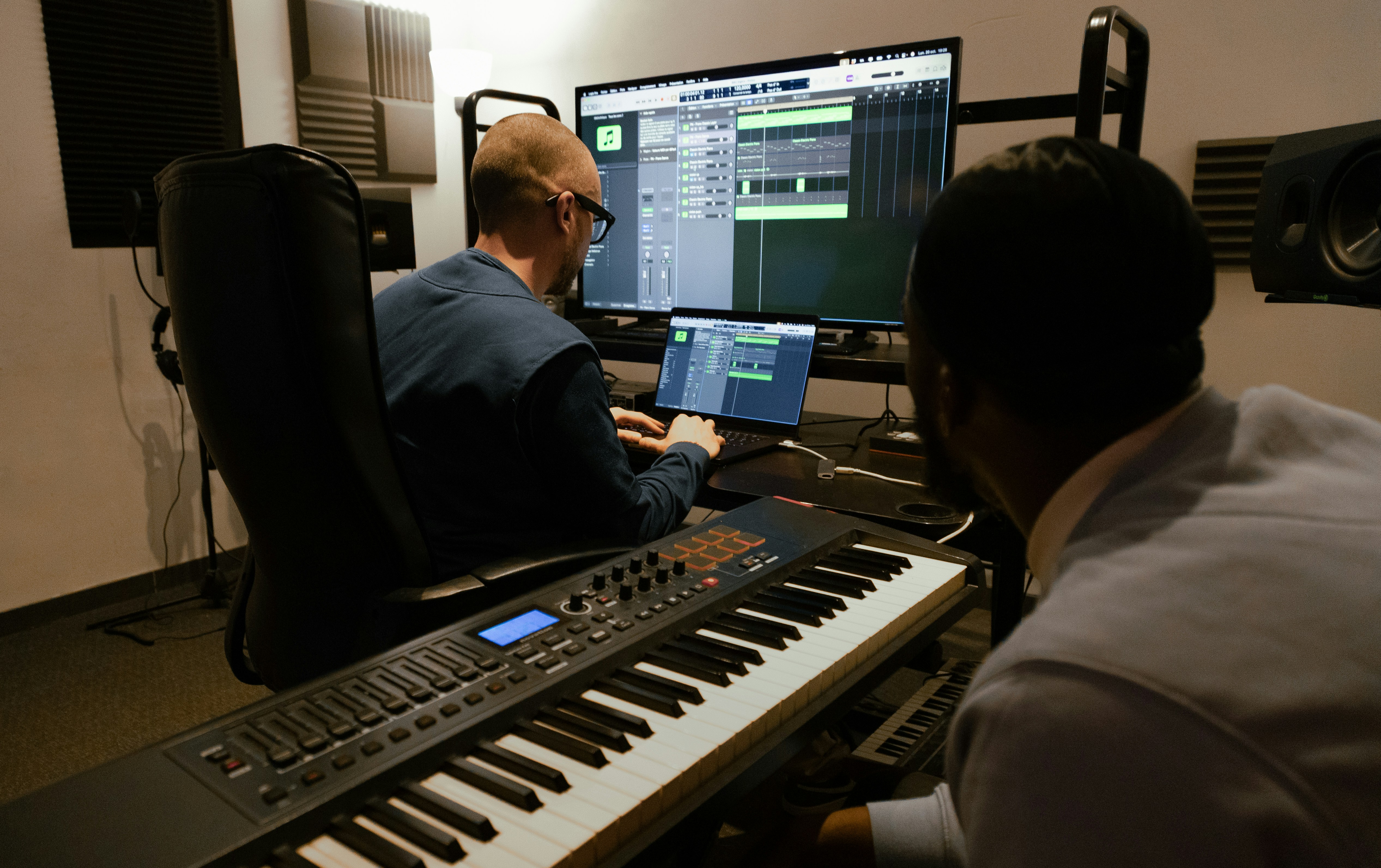 Two people producing music with a DAW and keyboard setup. Photo by Soundsitive Studio on Unsplash