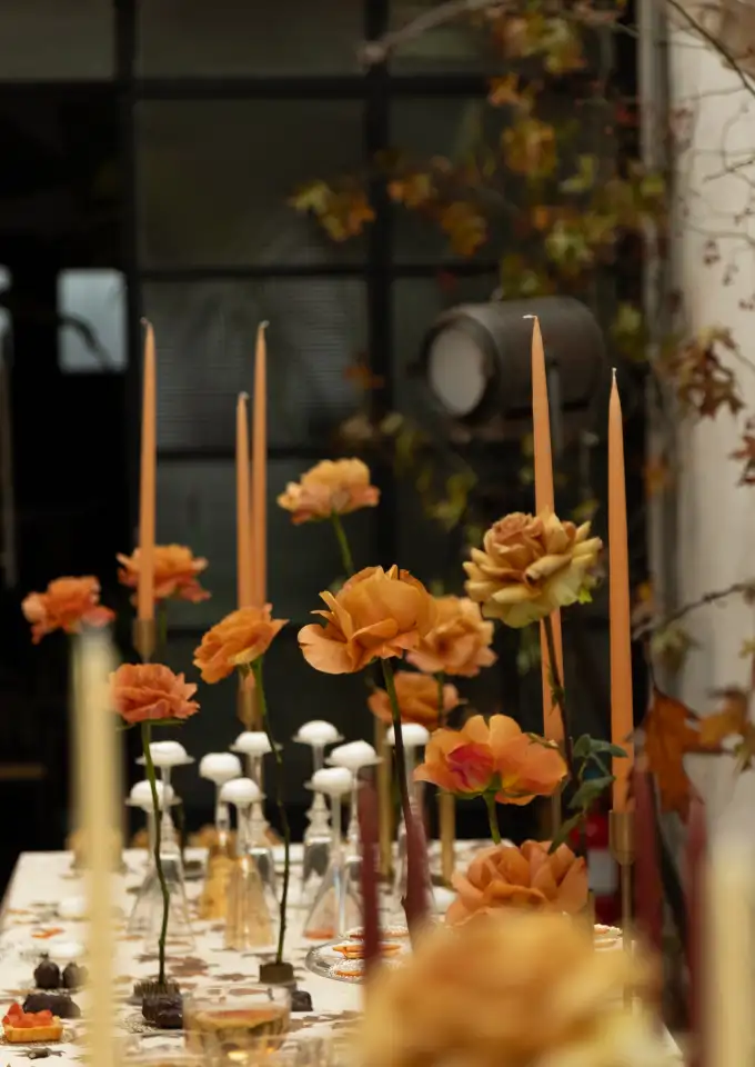 Mesa decorada con rosas ámbar y velas alargadas en tonos cálidos, diseño floral íntimo y atmosférico para evento elegante.