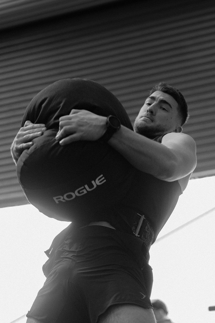 A man with defined abs holding onto a vertical pole in a gym, looking to the side.